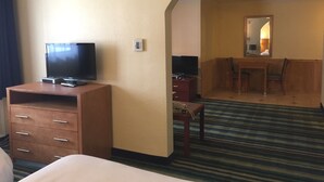 A hotel room with a bed, a television on a wooden stand, a desk with a chair, and a mirror on the wall.