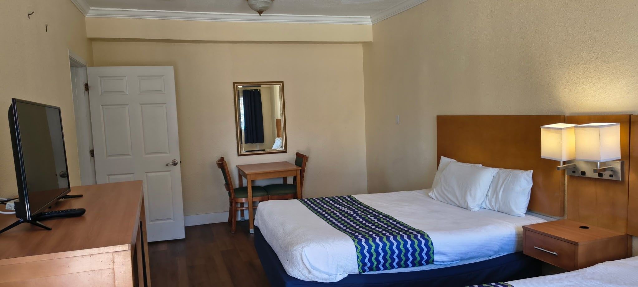 Une chambre d’hôtel comprenant un lit, une table de chevet, une lampe, un bureau, une chaise et un téléviseur.