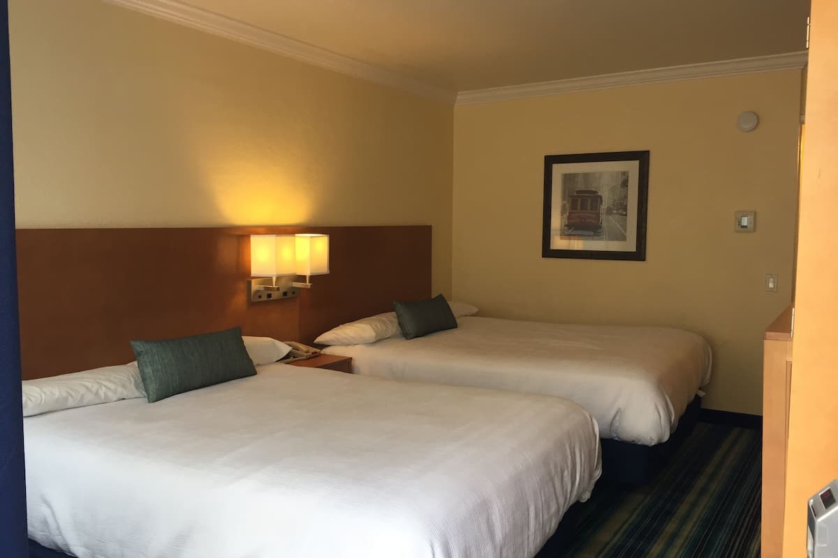 A hotel room with two beds, a nightstand, a wall-mounted lamp, and a framed picture.