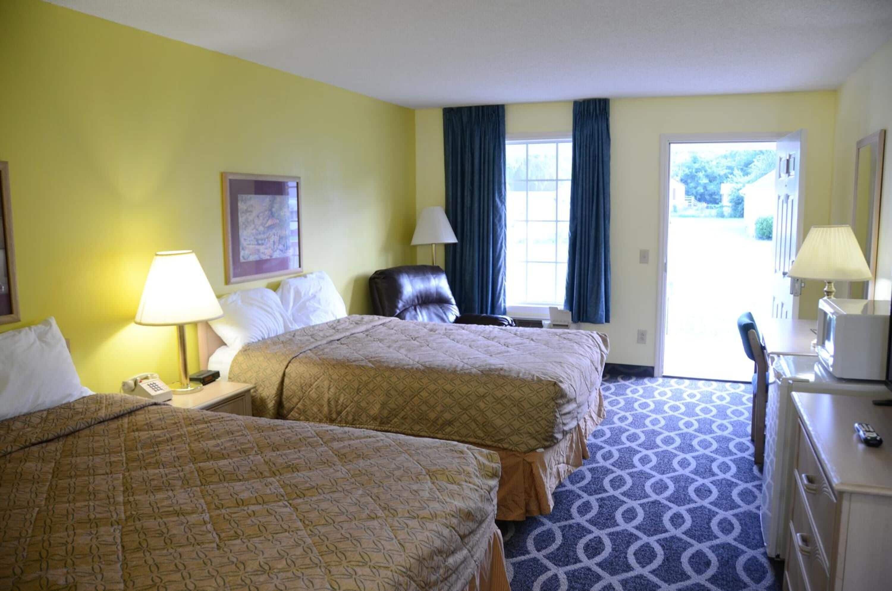 A hotel room with two beds, a desk, a chair, a lamp, and a window with curtains.