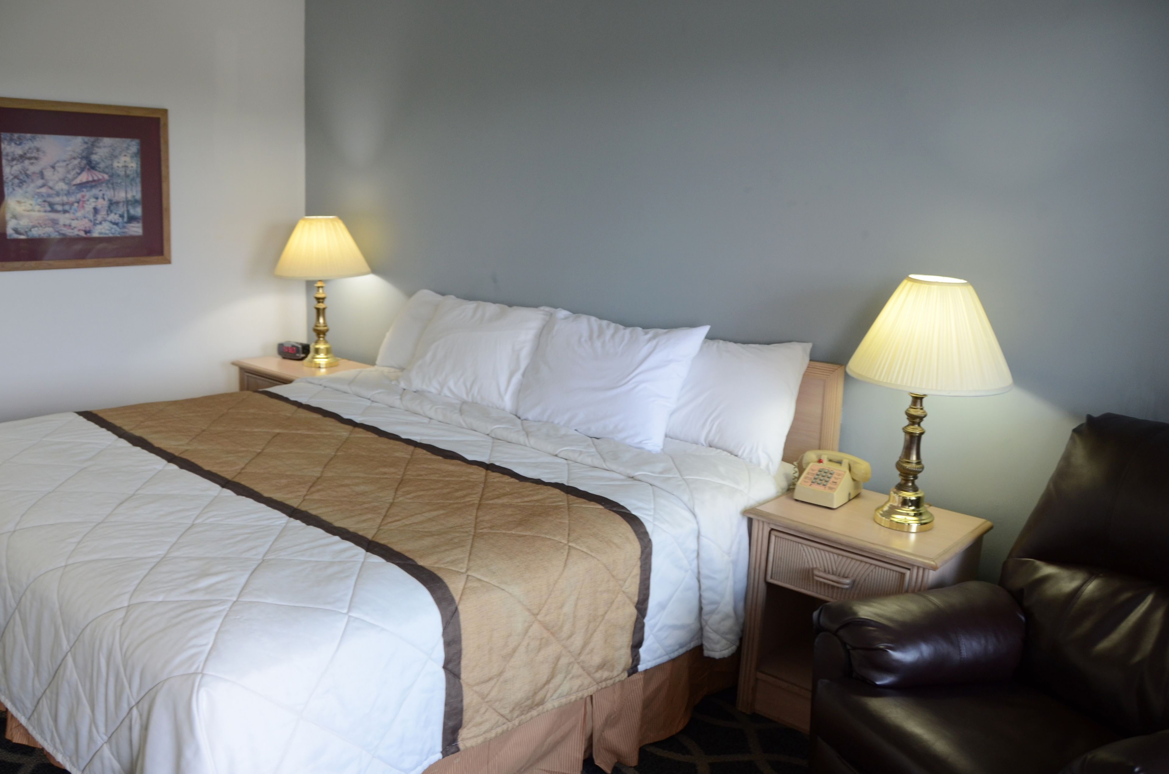 Un lit bien fait, recouvert d’une couverture matelassée, deux lampes de chevet, un téléphone et un fauteuil en cuir.