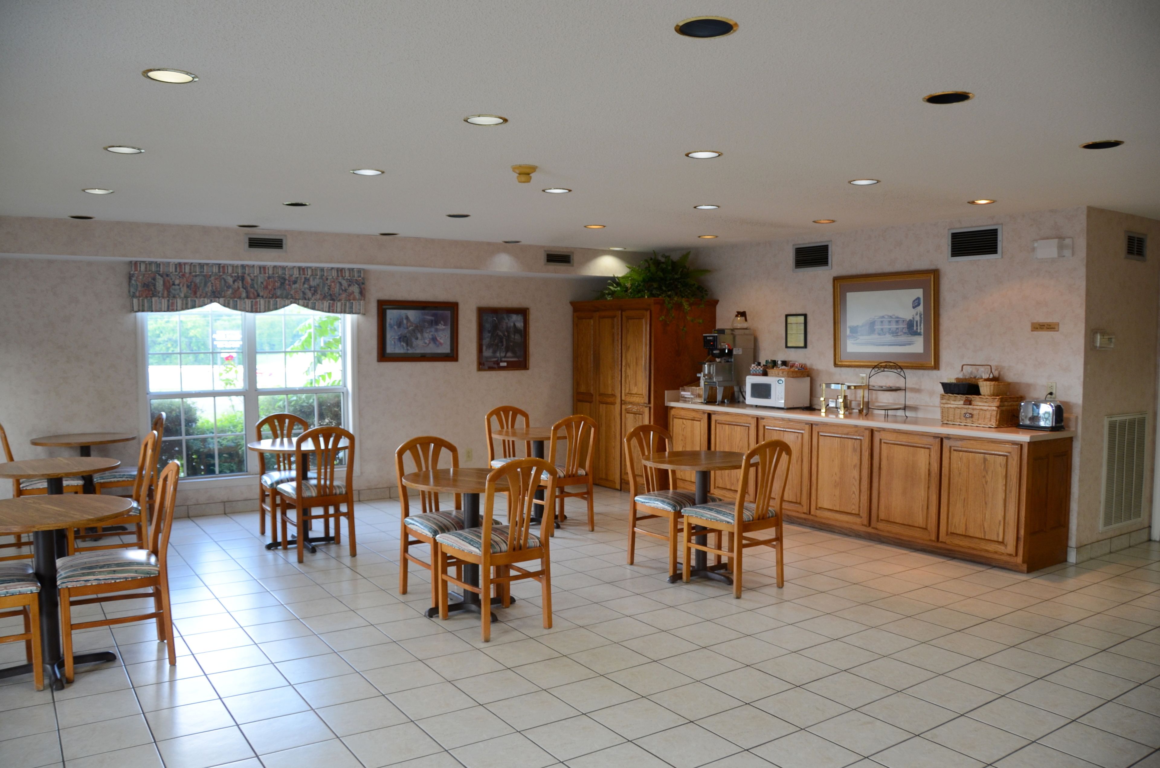 A spacious dining area with wooden tables and chairs, a kitchen with wooden cabinets, and a large window providing natural light.