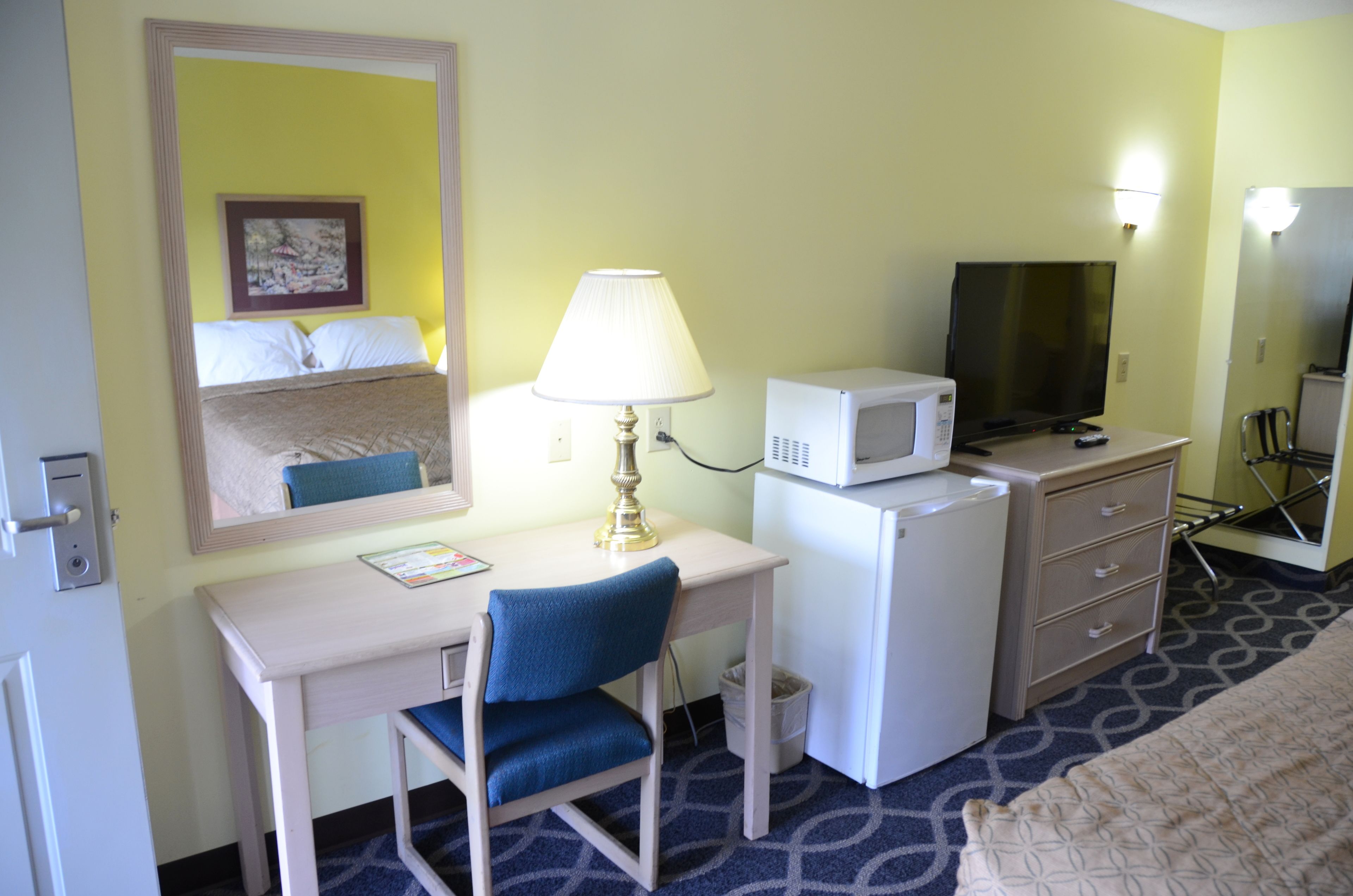 Een hotelkamer met een bureau, stoel, televisie, magnetron en een bed.