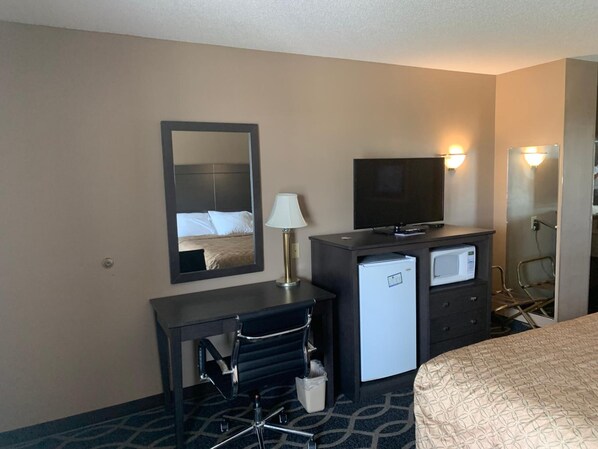 A hotel room with a bed, a desk with a chair, a television, a mini-fridge, a microwave, and a mirror.