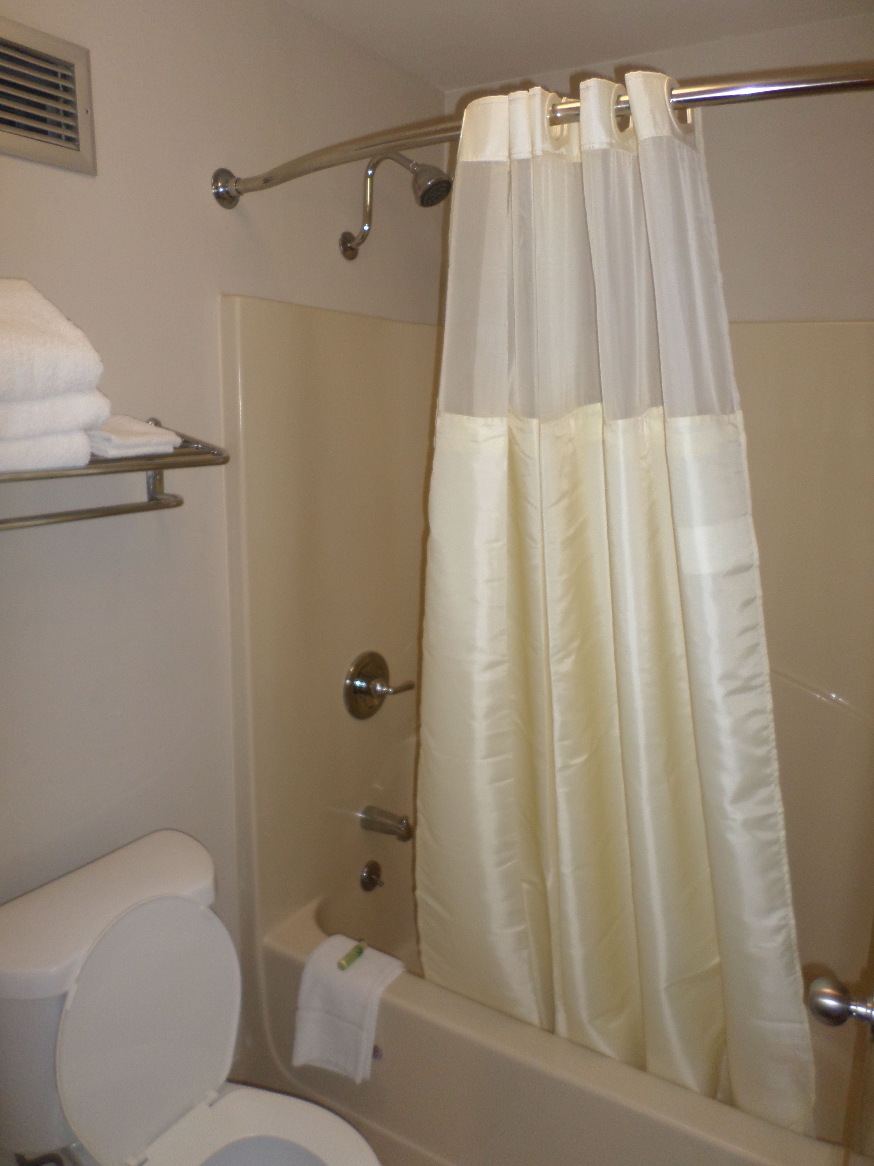 A bathroom with a shower curtain, a toilet, and a towel rack with folded towels.