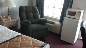 A hotel room with a bed, a green armchair, a bedside table with a lamp, a microwave, and a small refrigerator.