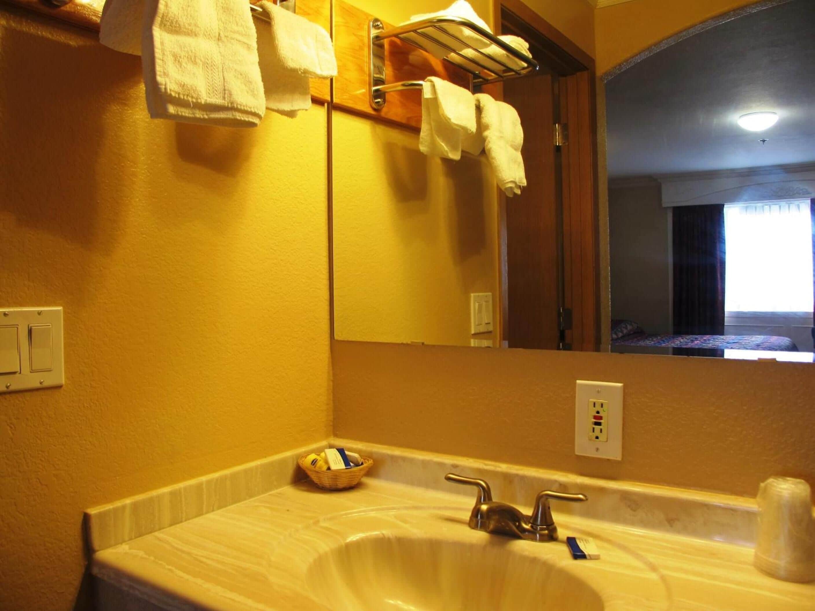 Ein Badezimmer mit Waschbecken, Spiegel, Handtuchhalter und einem kleinen Korb.