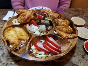 A wooden platter with various fried foods, including chicken wings, fish, and vegetables.