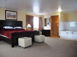 Habitación de hotel con una cama grande, dos mesitas de noche, una lámpara, un cuadro en la pared, un baño con bañera y zona de ducha.