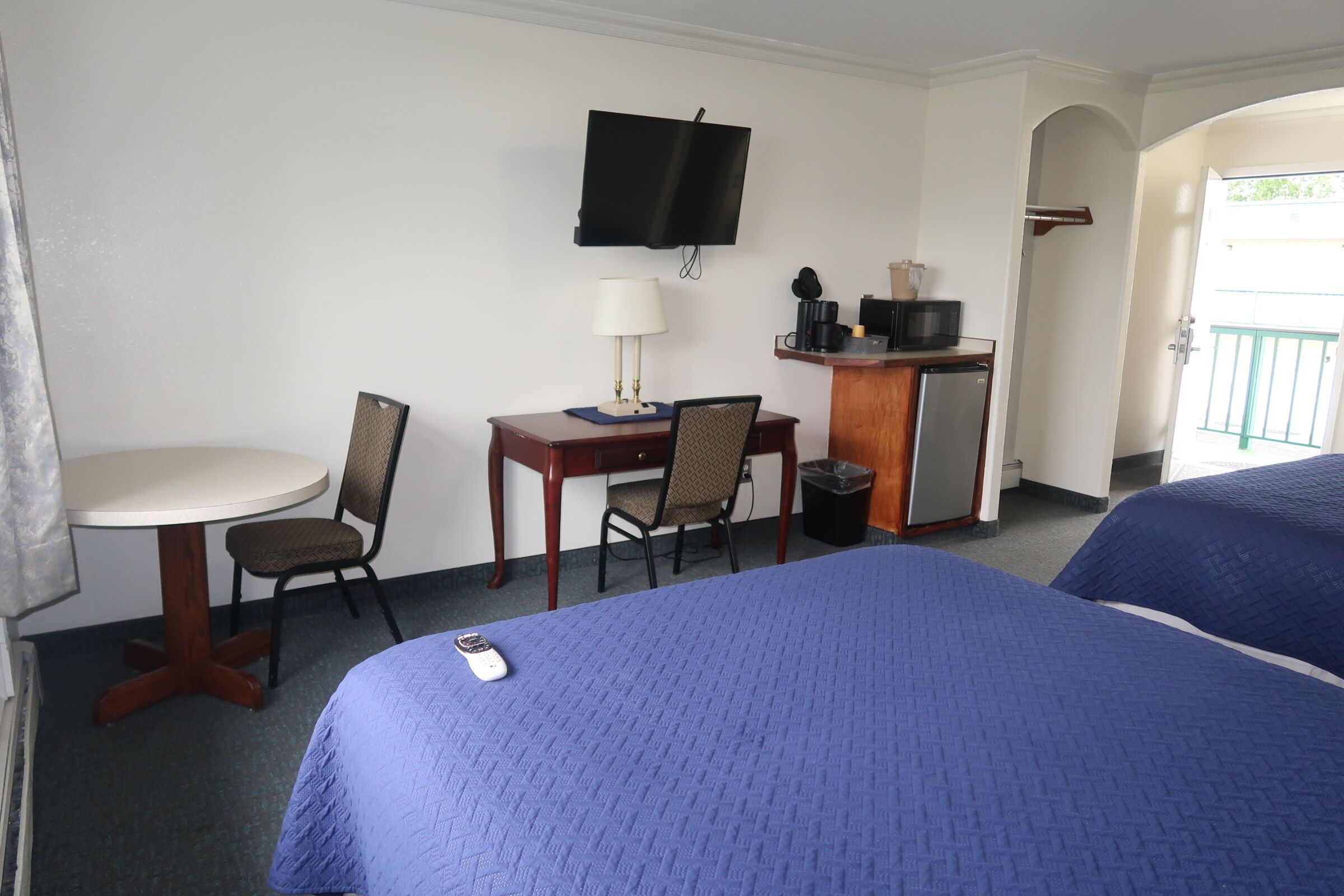 A hotel room with a bed, a desk with a chair, a television, and a small table with a lamp.