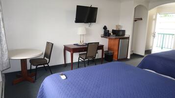 A hotel room with a bed, a desk with a chair, a television, and a small table with a lamp.