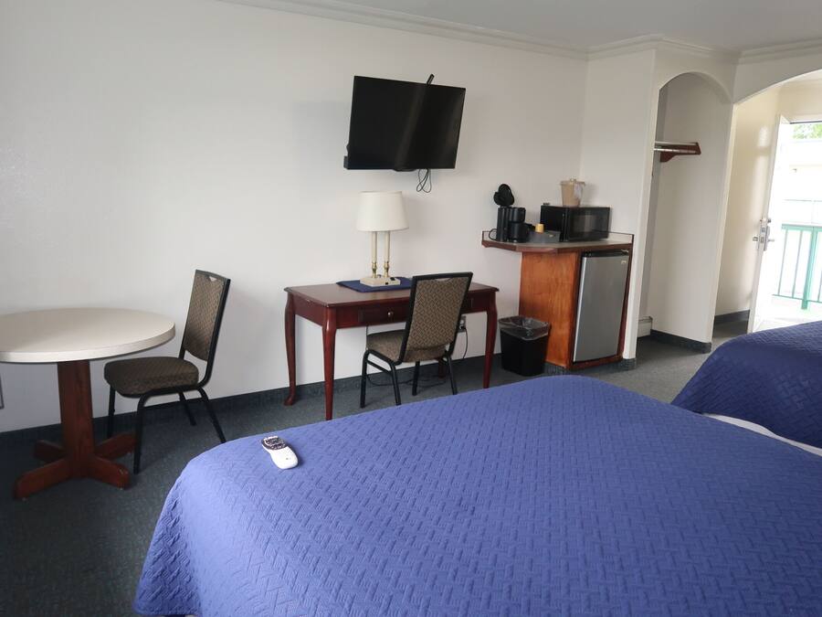 Habitación de hotel con una cama, un escritorio con silla, un televisor y una mesita de noche con lámpara.
