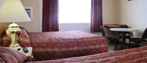 A hotel room with two beds, a desk, a chair, and a lamp.