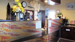 A reception area with a marble counter, a clock, a wall-mounted animal head sculpture, and a plant. - Merrill Field Inn (Anchorage)