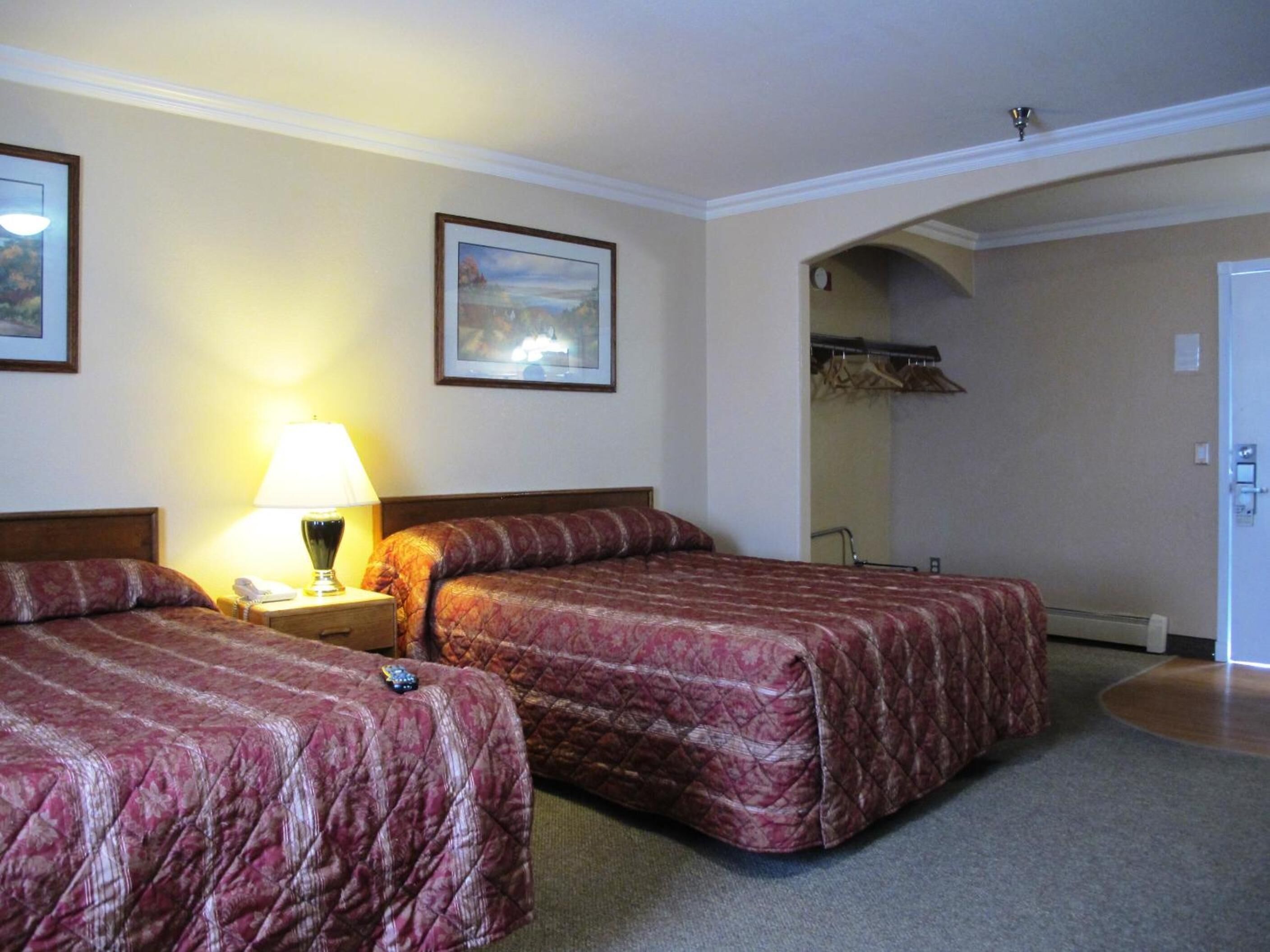 Una habitació d'hotel amb dos llits, una tauleta de nit amb una làmpada, un quadre amb marc a la paret i una porta que condueix a un bany.
