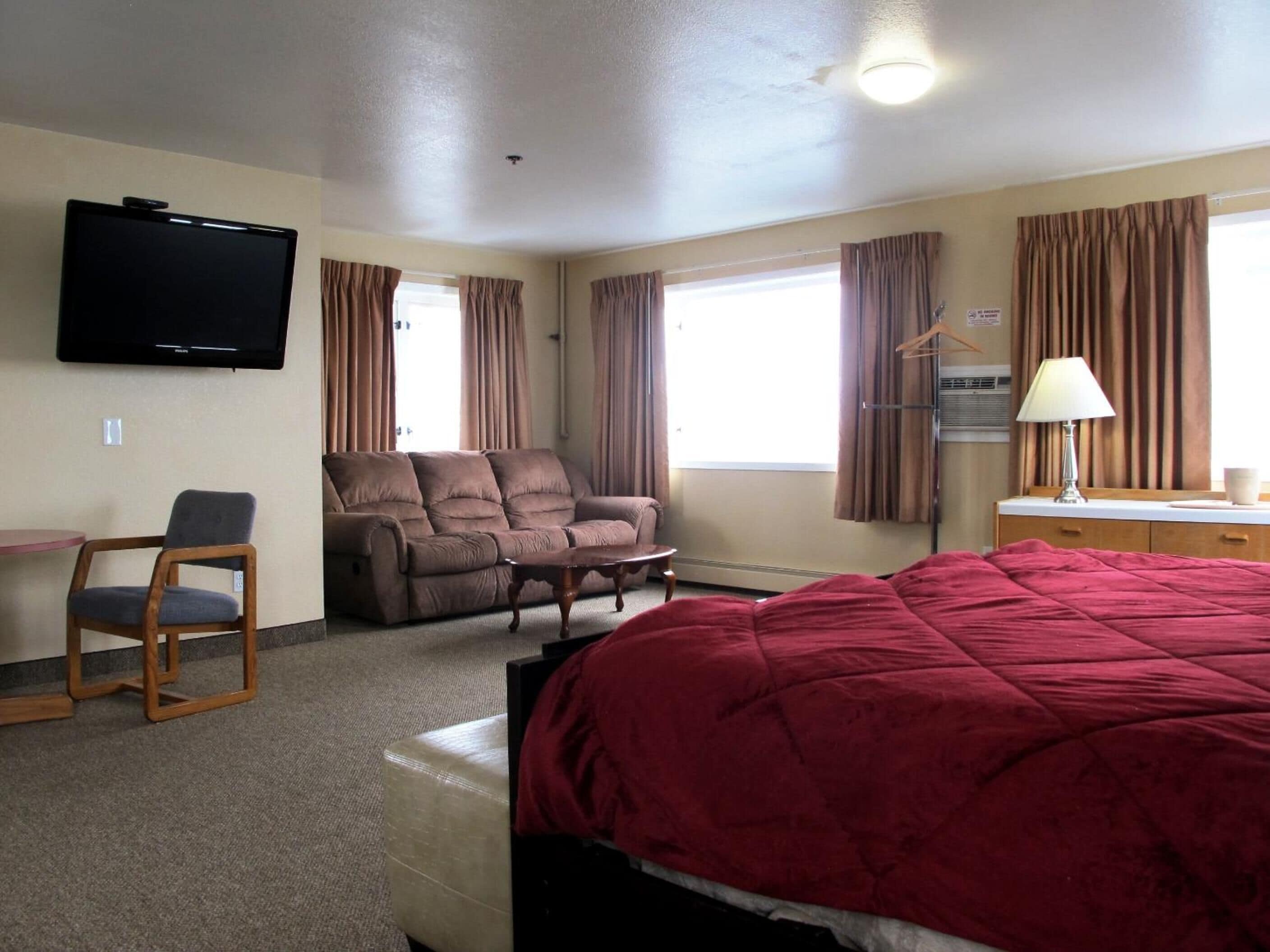 Ein Hotelzimmer mit Bett, Sofa, Sessel, Fernseher und Schreibtisch.