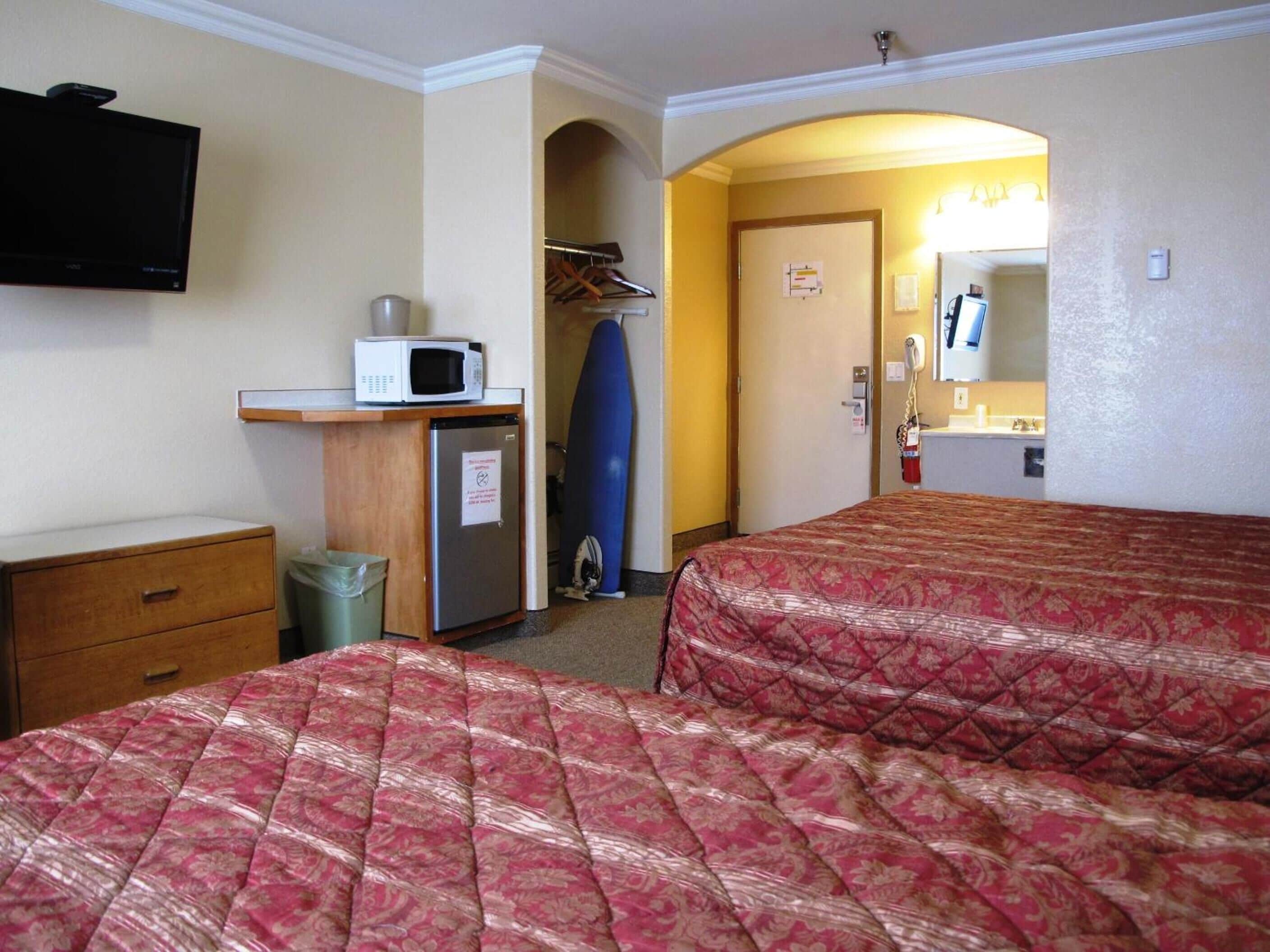 Une chambre d’hôtel avec deux lits, un four à micro-ondes, un petit réfrigérateur, une poubelle, une armoire avec des vêtements et une porte donnant sur une salle de bain.