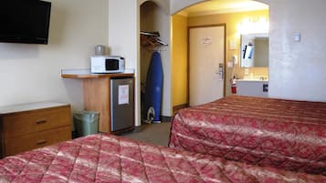 A hotel room with two beds, a microwave, a small refrigerator, a trash bin, a closet with clothes, and a door leading to a bathroom.