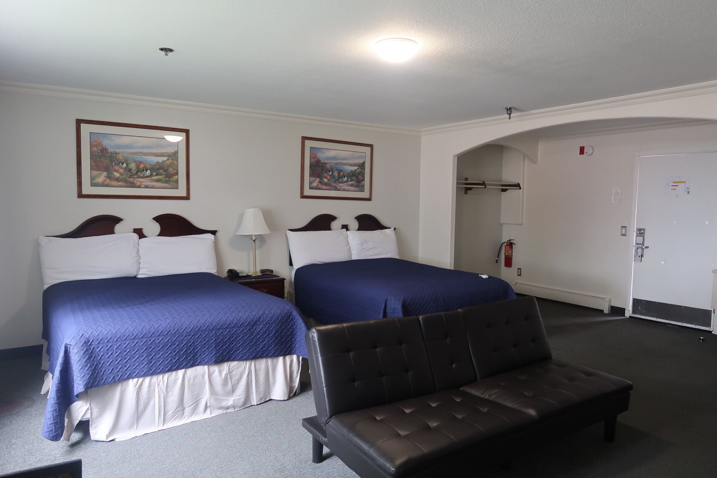 Habitación de hotel con dos camas, un banco, una mesita de noche, una lámpara y dos cuadros en la pared.