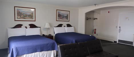 Habitación de hotel con dos camas, un banco, una mesita de noche, una lámpara y dos cuadros en la pared.