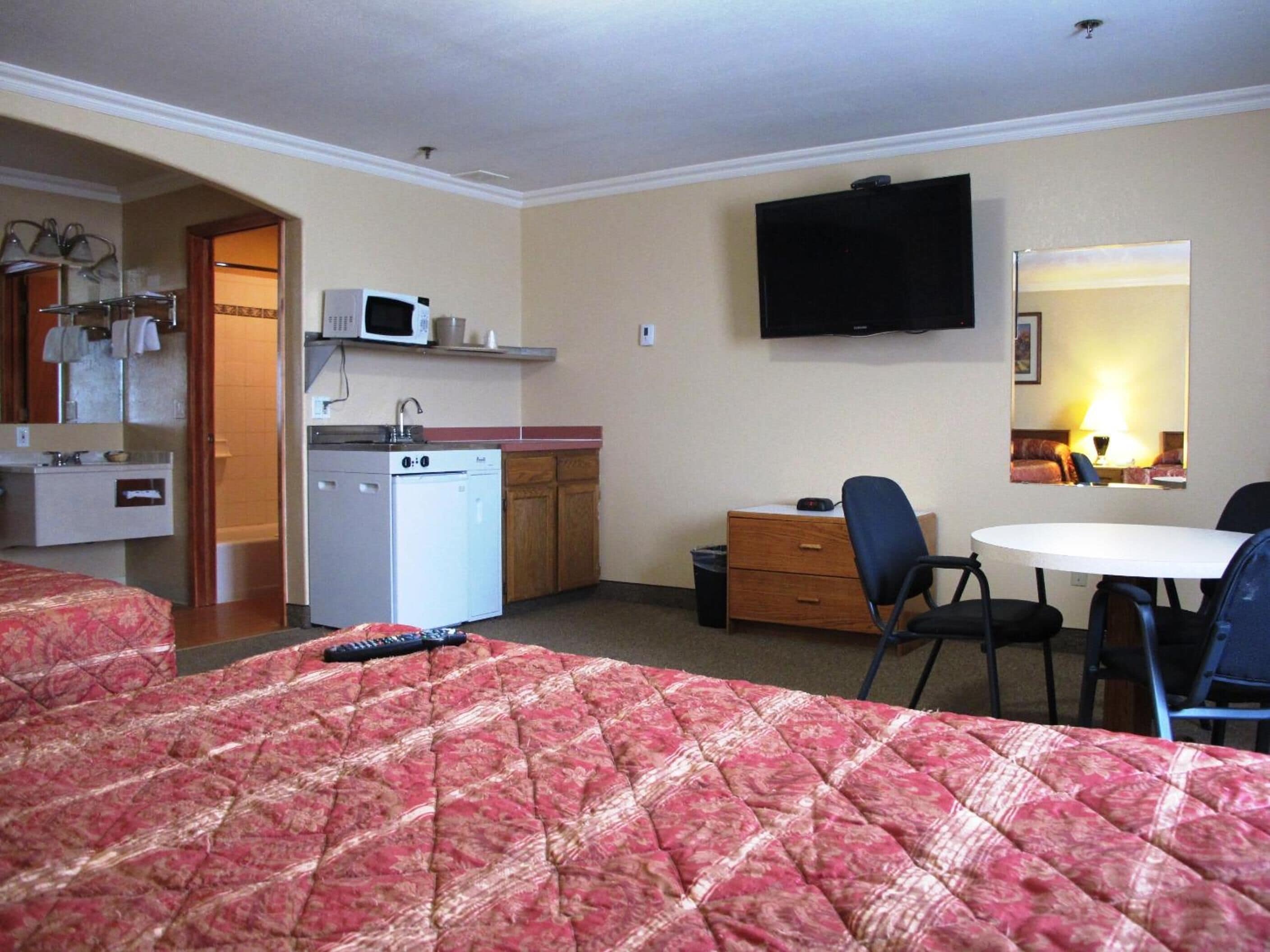 Una camera d'albergo con un letto, una scrivania, una sedia, una televisione, un forno a microonde, un lavandino e un angolo cottura.