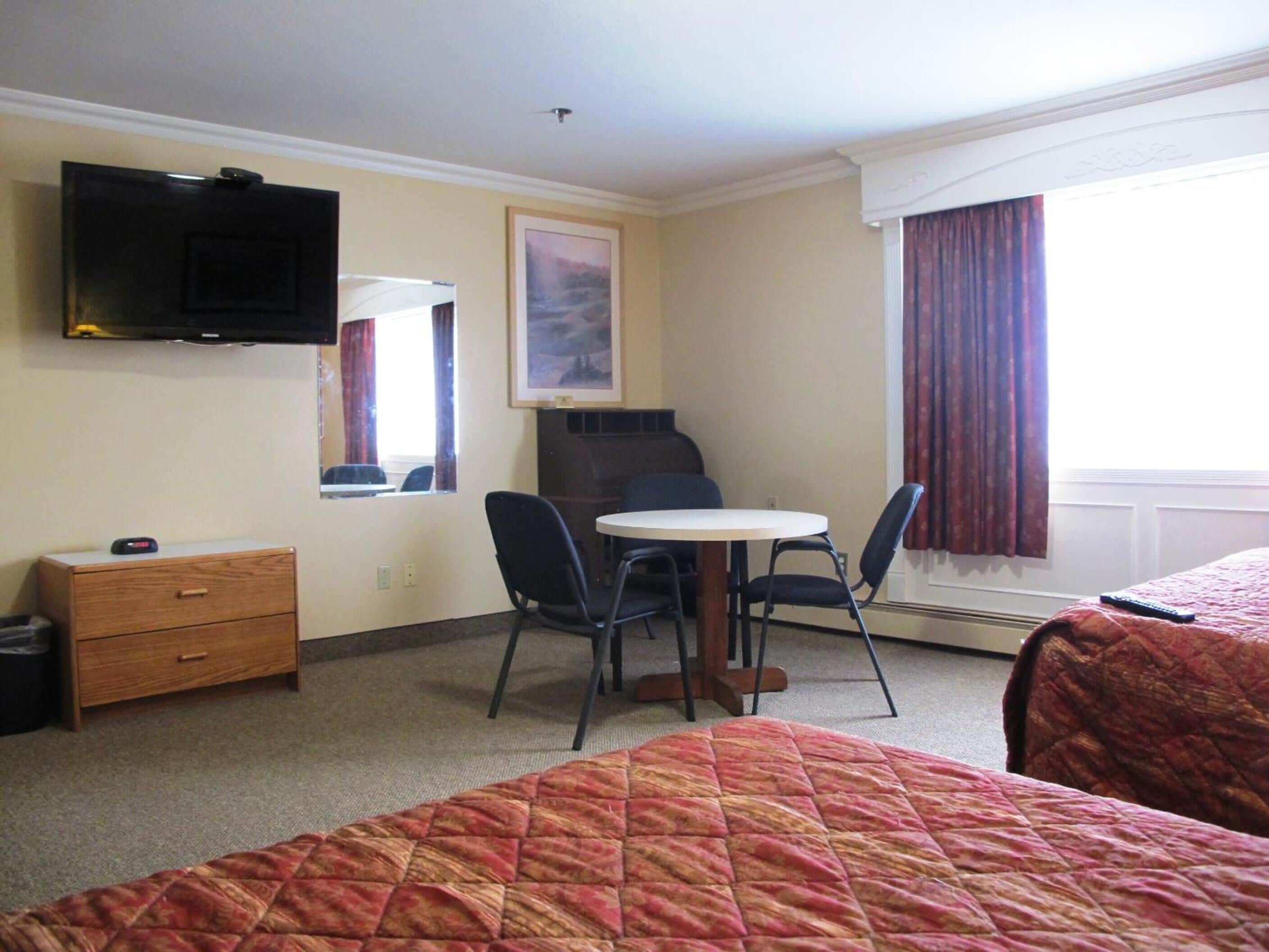 Une chambre d’hôtel avec deux lits, un bureau avec une chaise, un téléviseur fixé au mur, une fenêtre avec des rideaux et un tableau au mur.