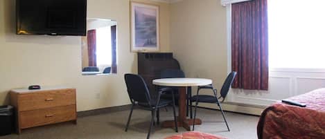 Een hotelkamer met twee bedden, een bureau met stoel, een aan de muur bevestigde televisie, een raam met gordijnen en een schilderij.