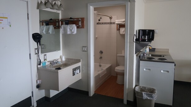 Un baño pequeño y funcional con lavamanos, espejo, toallero, ducha, inodoro y una kitchenette con cafetera.
