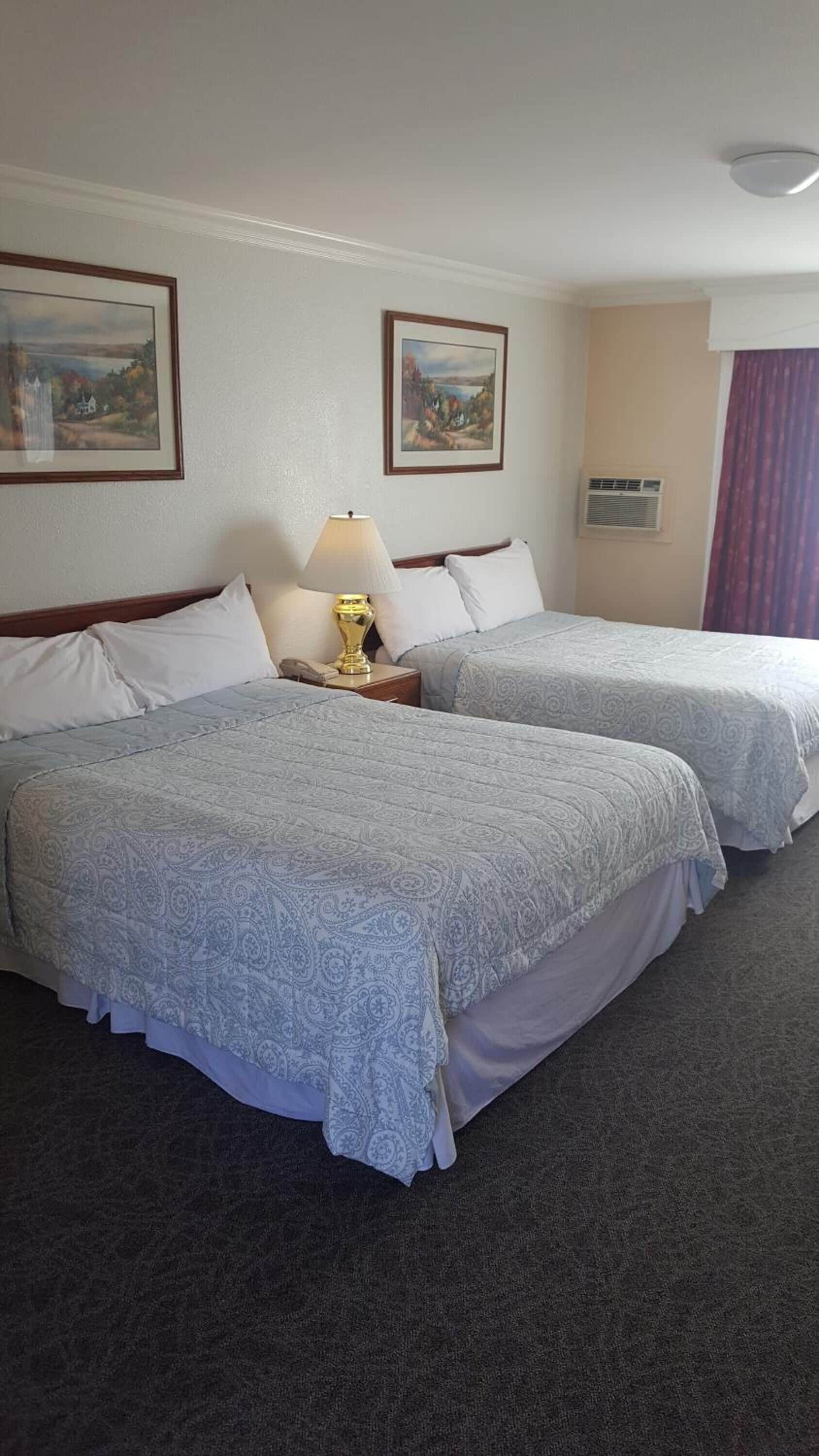 A hotel room with two beds, a nightstand with a lamp, and two framed pictures on the wall.