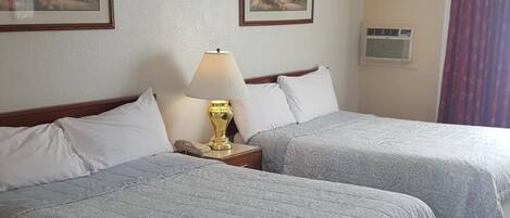 A hotel room with two beds, a nightstand with a lamp, and two framed pictures on the wall.