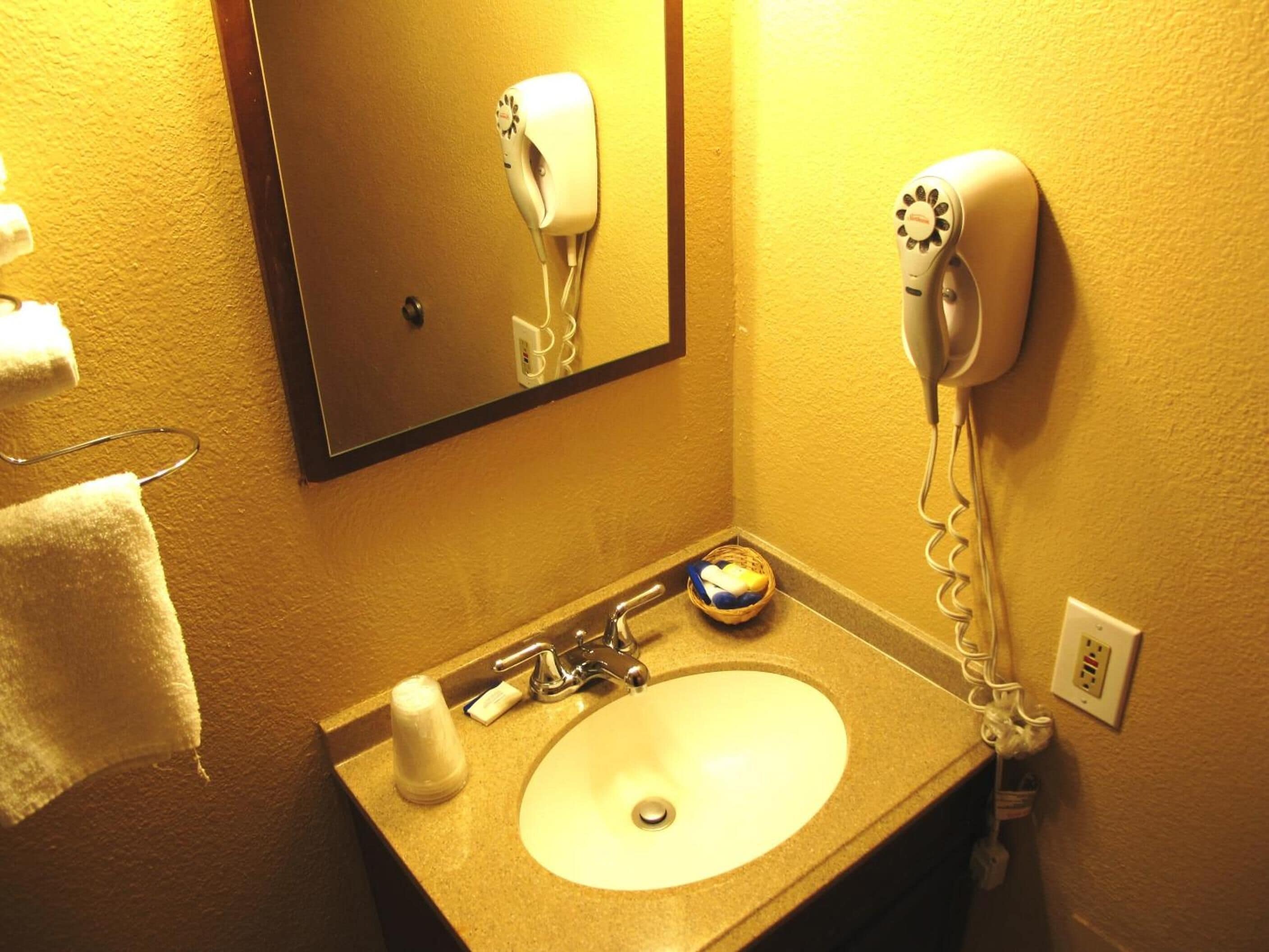 A bathroom with a sink, a hairdryer, and a mirror.