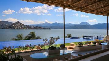 Una terraza con vistas a un lago y montañas, con mobiliario exterior y una mesa de vidrio.