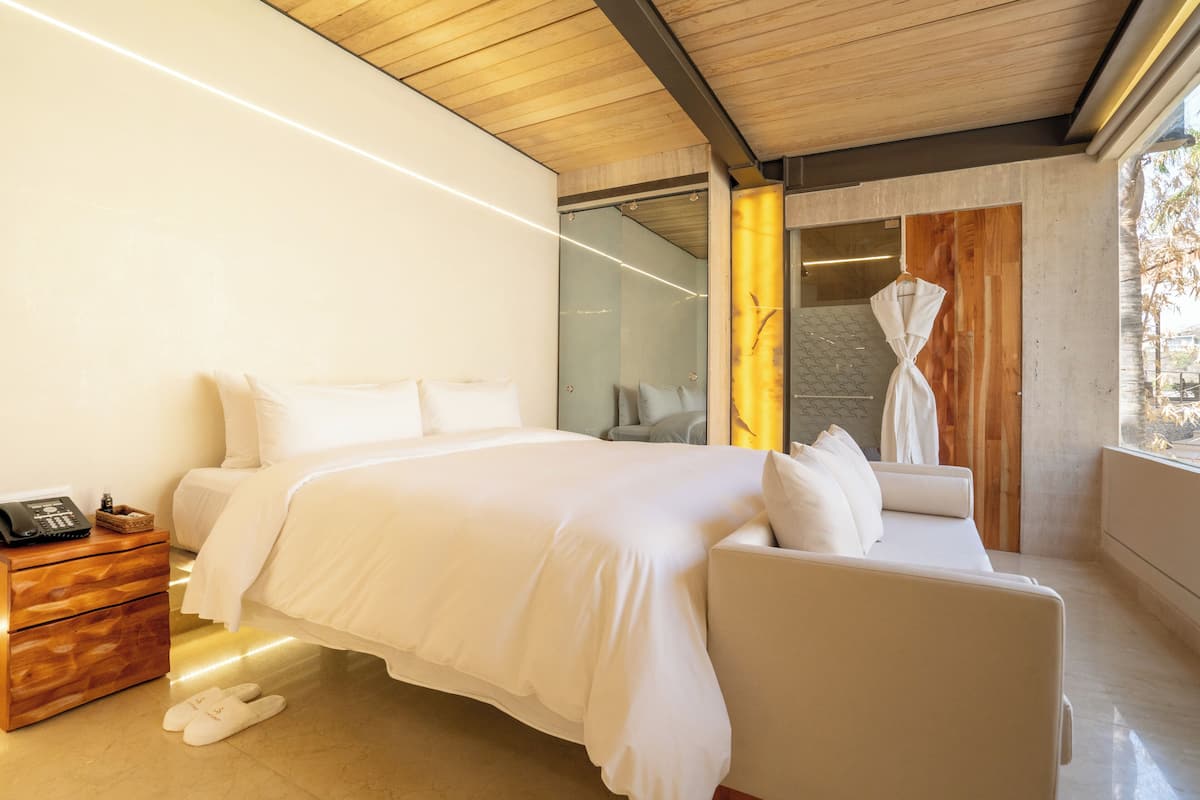 Ein modernes Schlafzimmer mit einem großen Bett, einem Nachttisch aus Holz, einem Bademantel und Blick ins Freie.