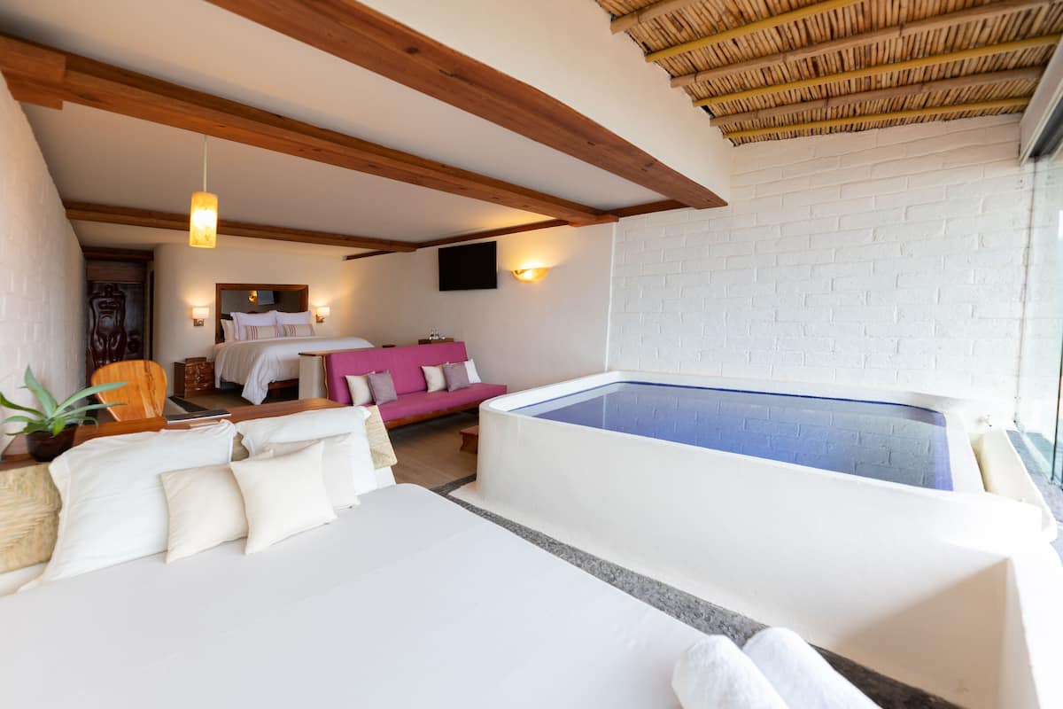 Ein Schlafzimmer mit einem großen Bett, einer kleinen Couch, einem an der Wand montierten Fernseher und einer Whirlwanne.
