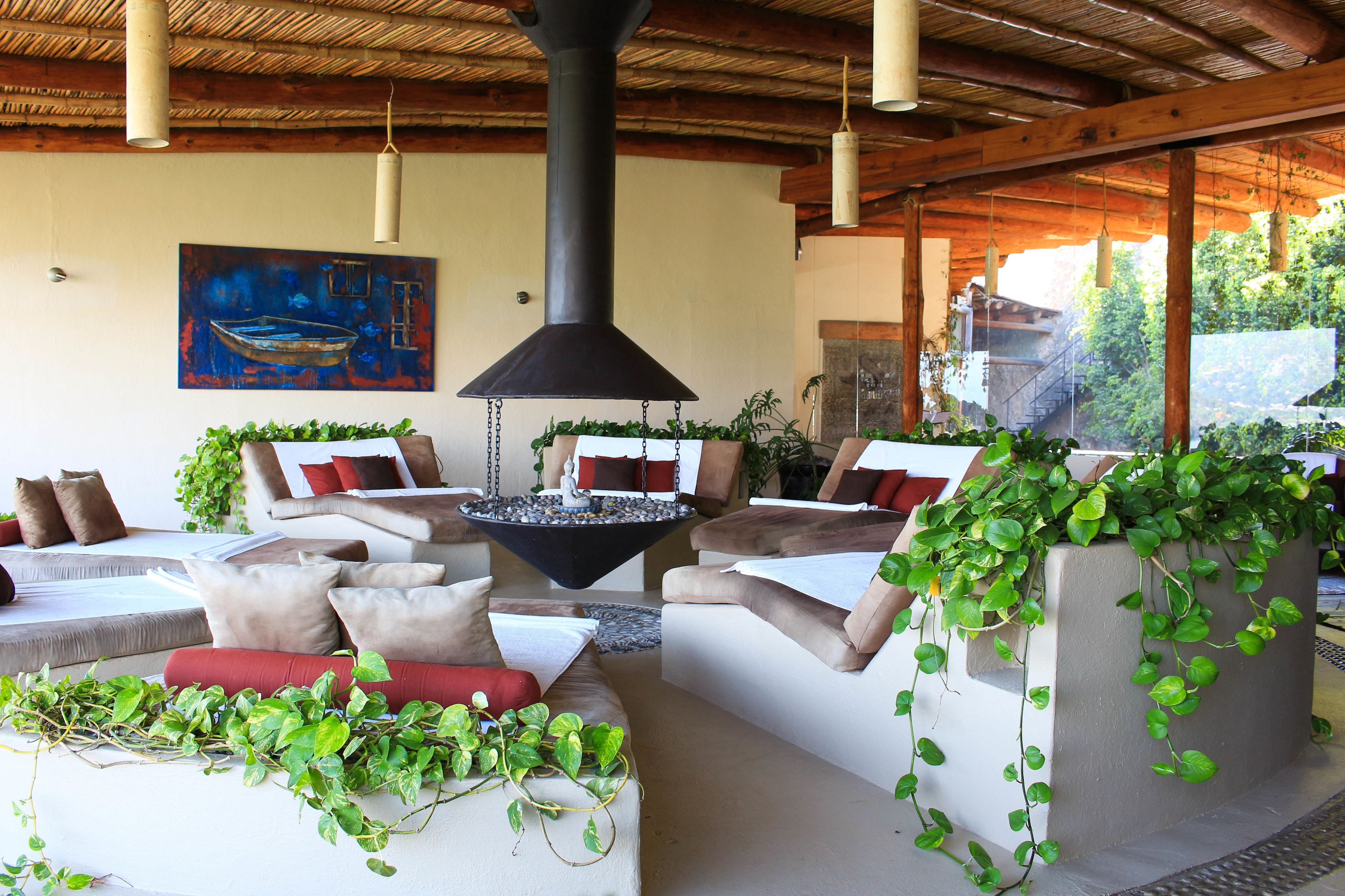 A modern lounge area with comfortable seating, a central fire feature, and lush greenery.