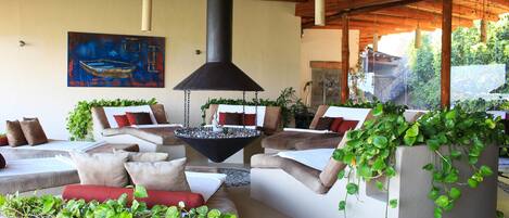 A modern lounge area with comfortable seating, a central fire feature, and lush greenery.