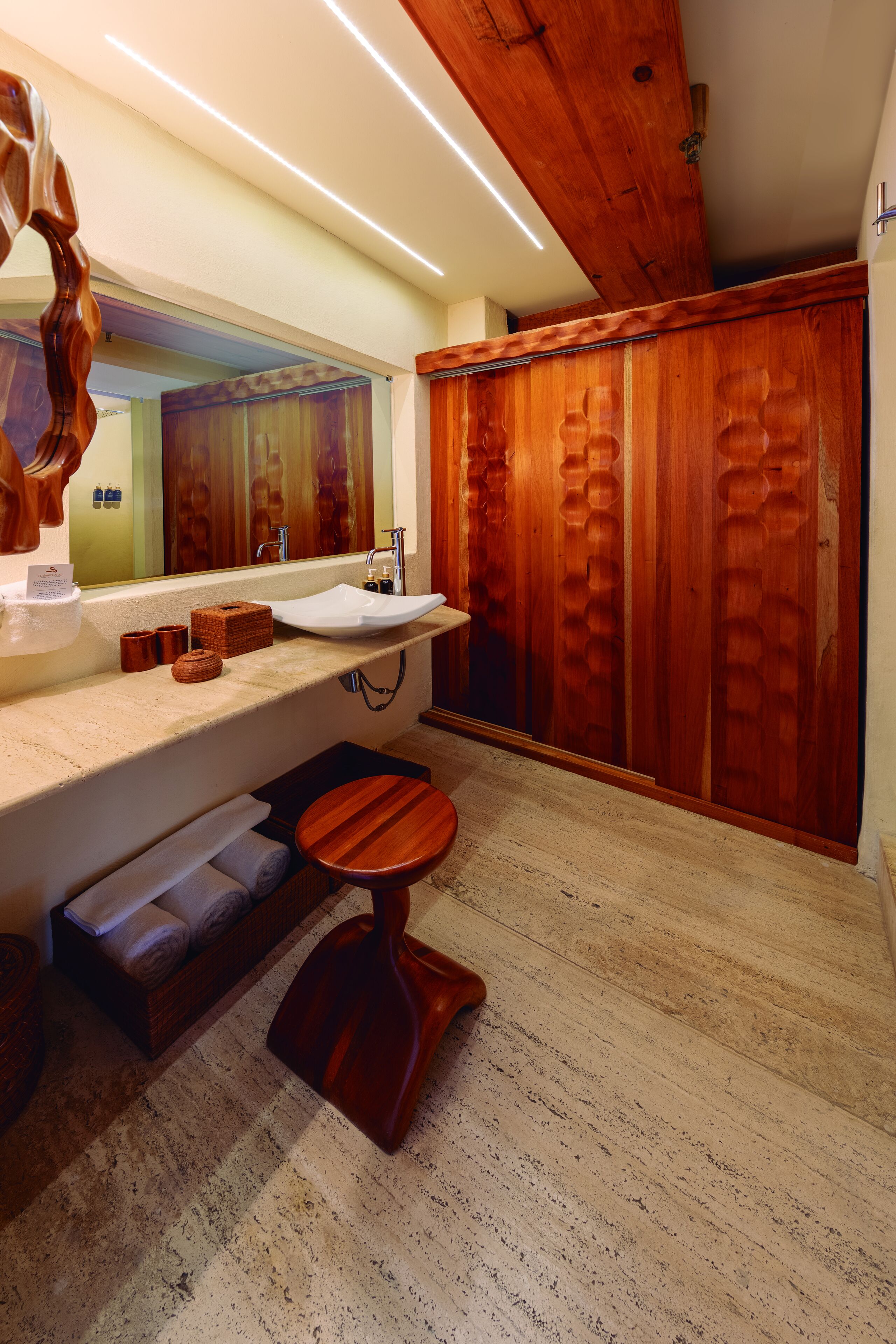 A modern bathroom with a wooden vanity, a large mirror, a sink, and a wooden stool.