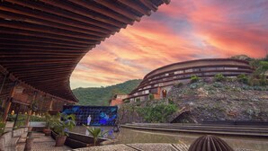 A modern building with a curved roof, surrounded by lush greenery and a scenic sunset. - El Santuario Resort & Spa (Valle de Bravo)