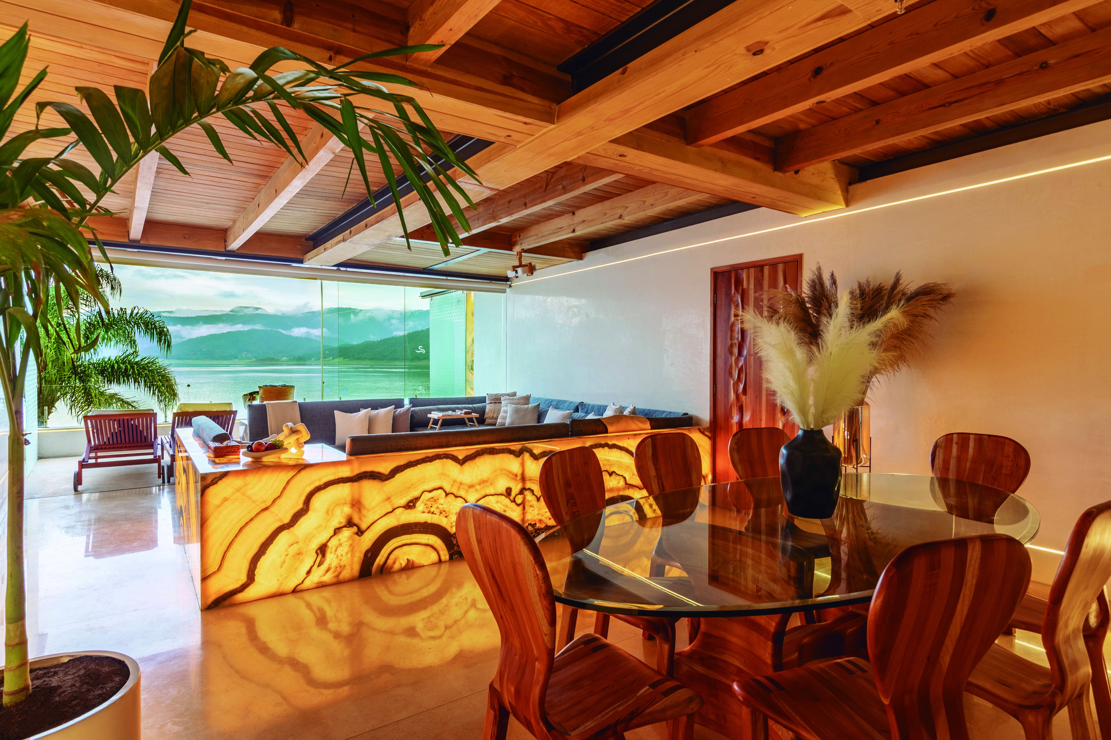 A modern dining area with a glass table and wooden chairs, a wooden reception desk, and a view of the outdoors.