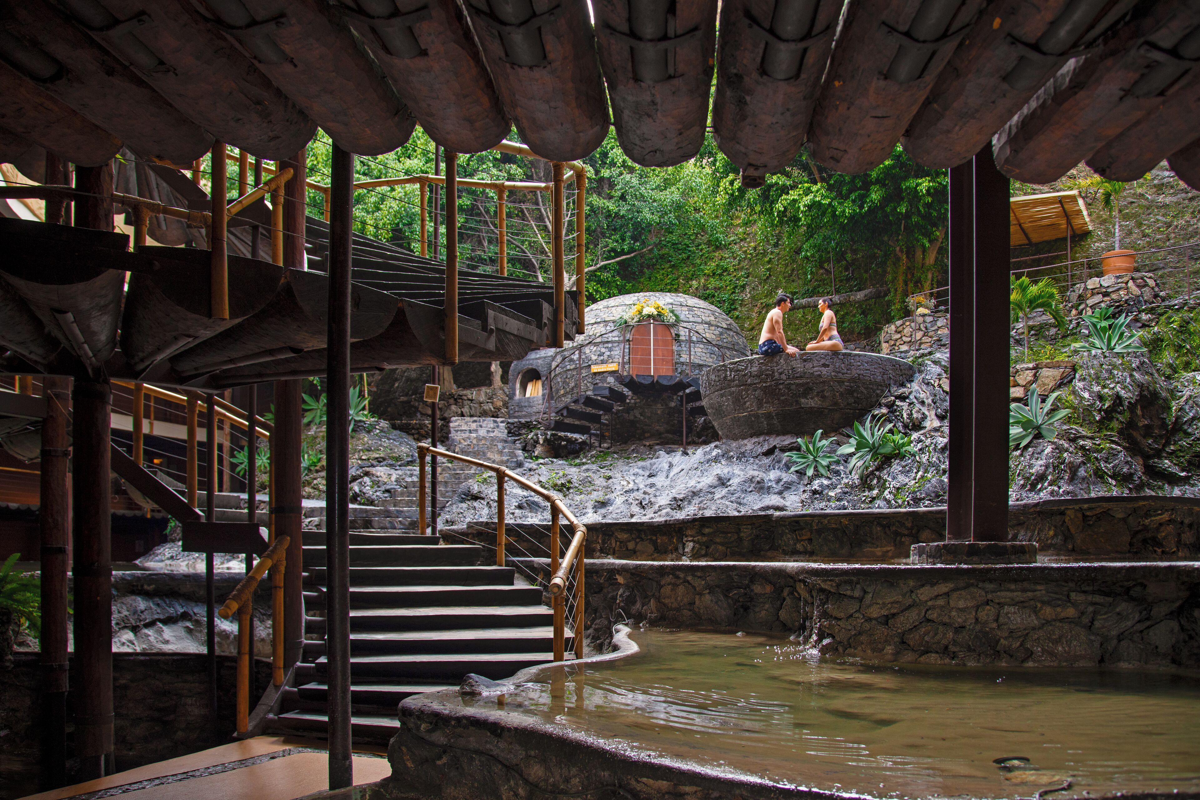 A traditional bamboo staircase leading to a stone platform with a small pond.