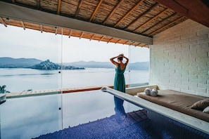 Quarto com piscina infinita de vidro, vista para um lago e teto de madeira.