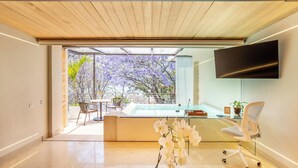 A modern room with a glass door leading to a balcony, a flat-screen TV mounted on the wall, and a seating area with a table and chairs. - El Santuario Resort & Spa (Valle de Bravo)