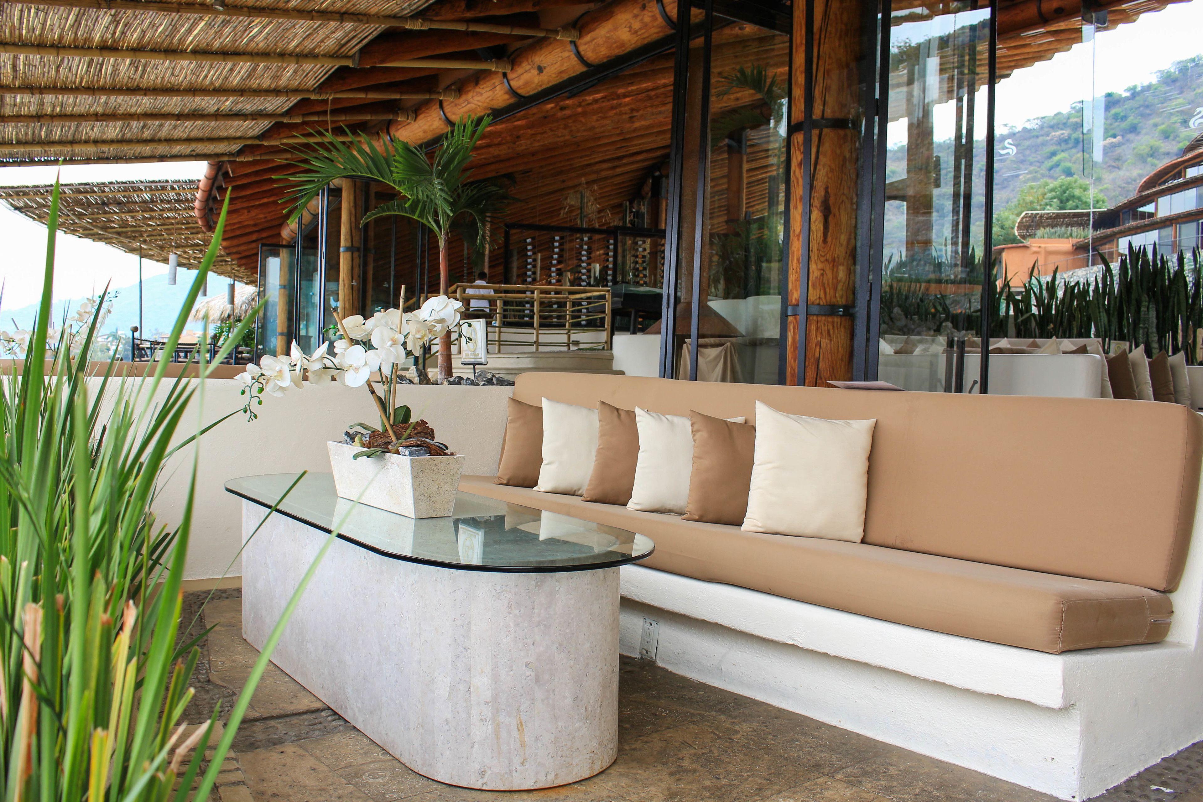 A modern outdoor seating area with a glass-top coffee table, beige sofa, and potted plants.