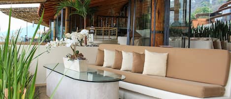 A modern outdoor seating area with a glass-top coffee table, beige sofa, and potted plants.