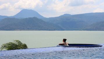 Una persona relajándose en una piscina con vistas a montañas y una masa de agua.