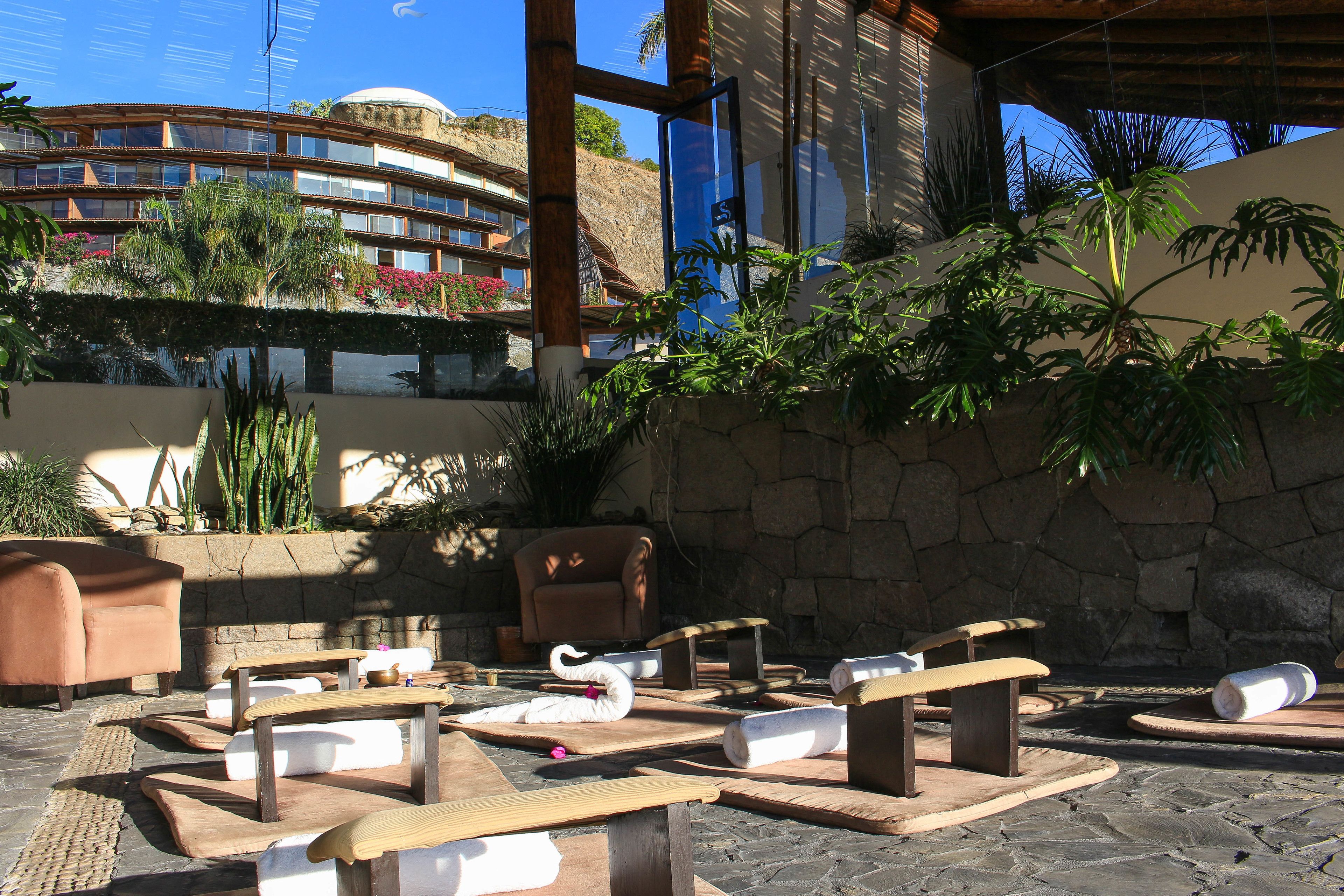Un espace extérieur aménagé avec des tables et des bancs en bois, des coussins en forme de cygne et un mur en pierre en arrière-plan.