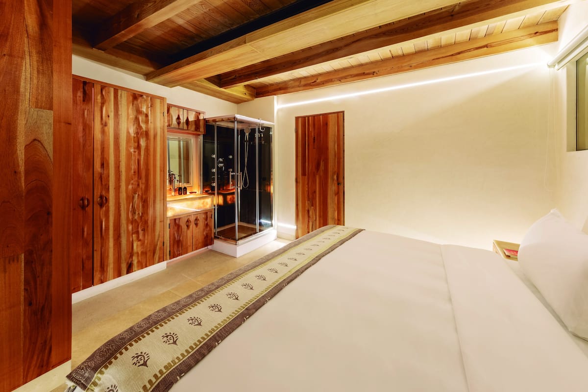Ein Schlafzimmer mit Holzboden, einem großen Bett, einem Holzschrank und einer Duschkabine aus Glas.