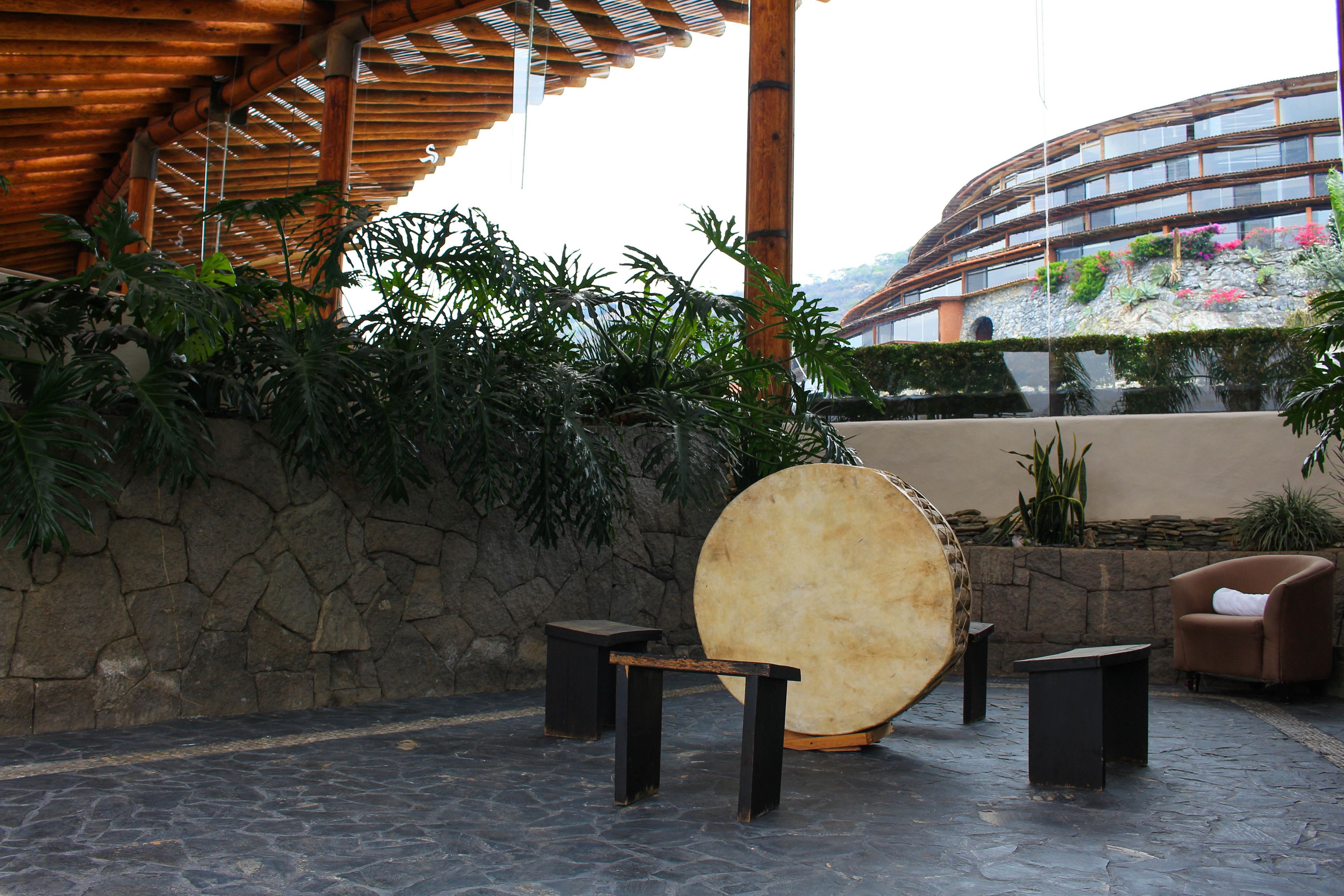 An outdoor patio area with a stone wall, a large drum, and a modern building in the background.