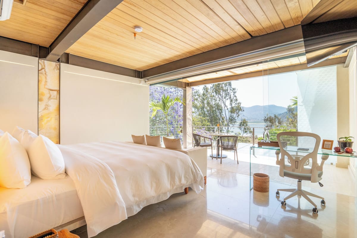 Ein modernes Schlafzimmer mit einem großen Bett, einem verglasten Balkon und Blick ins Freie.