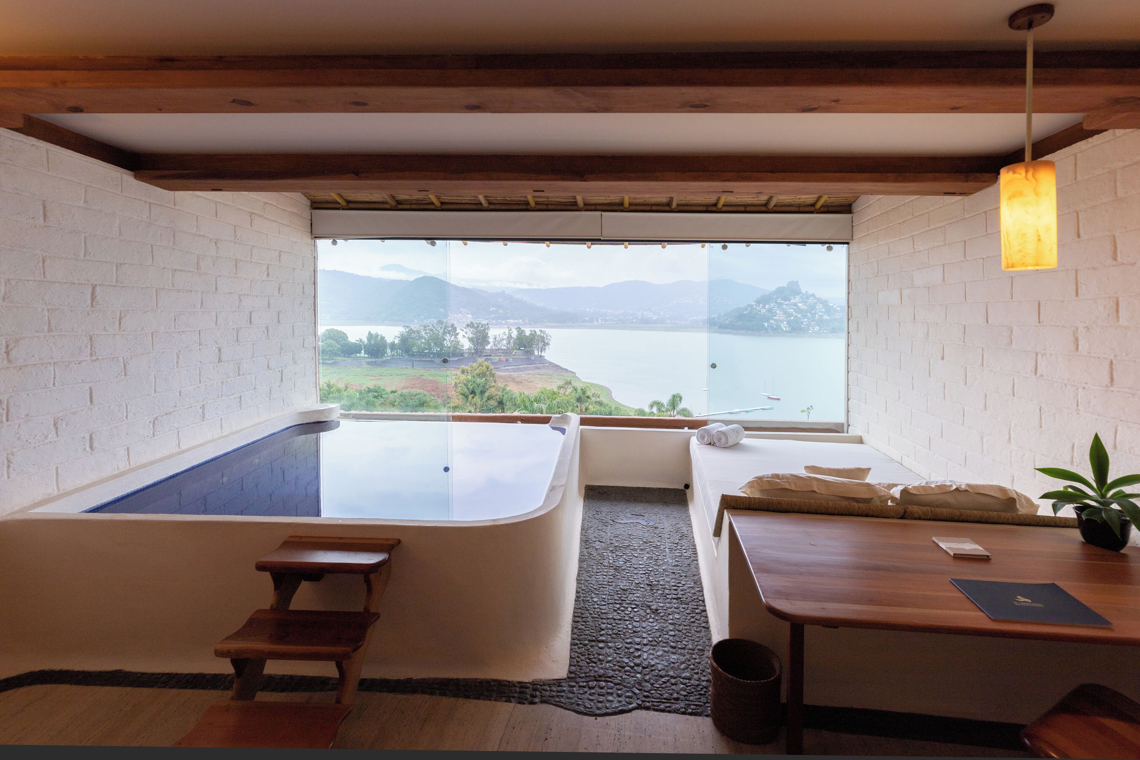 Ein Spa-Raum mit Whirlpool, einer Holzbank und Blick auf einen See und Berge.
